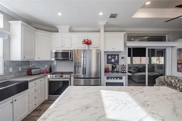 a kitchen with stainless steel appliances kitchen island granite countertop a refrigerator oven a sink dishwasher and white cabinets with wooden floor