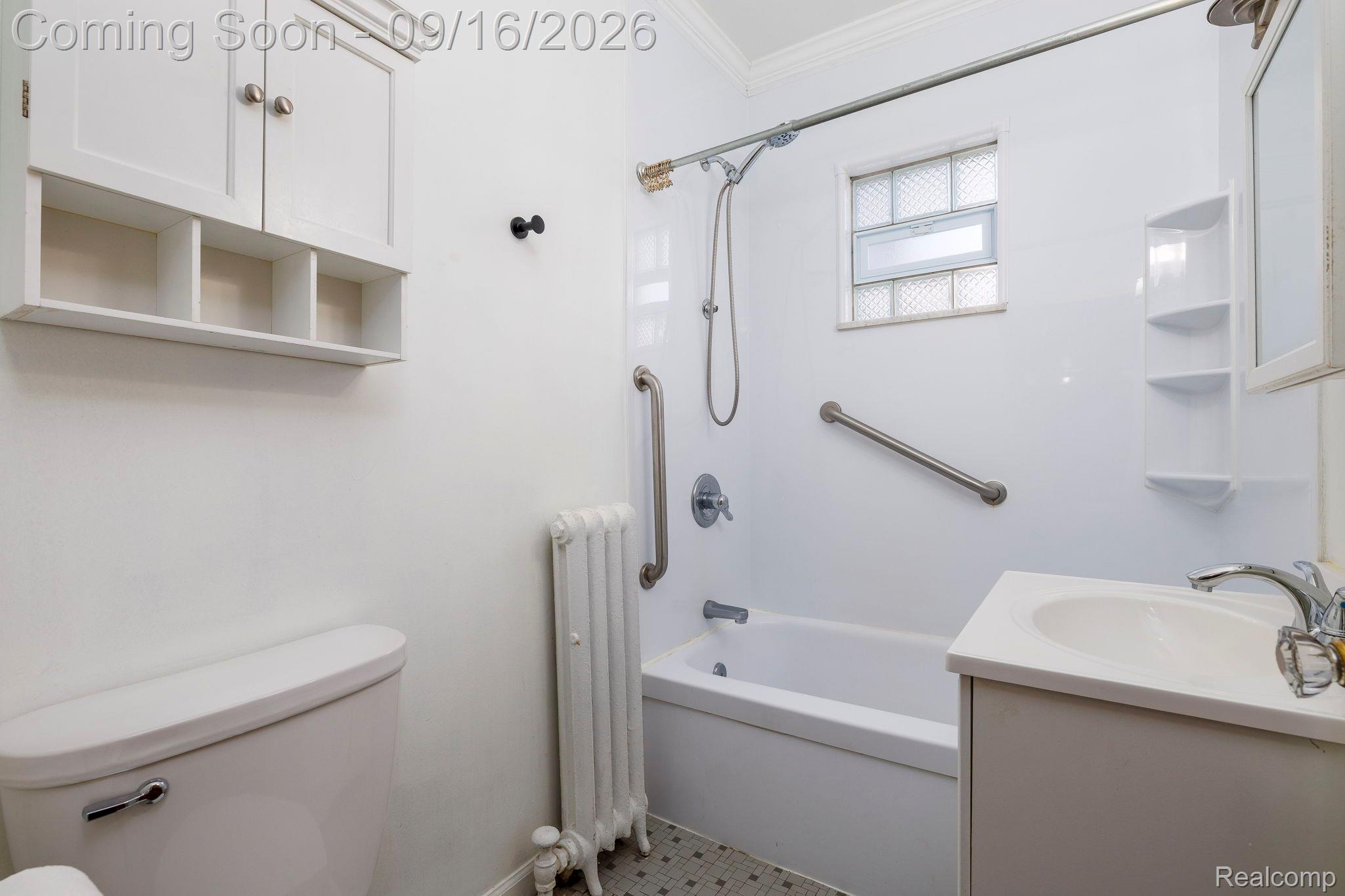 999 Nottingham Road Grosse Pointe, MI 48230 - Photo 23 of 30 Bathroom featuring a white vanity with a built-in sink, a bathtub with a shower, a wall-mounted storage cabinet, and a glass block window