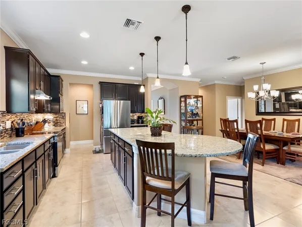 a kitchen with stainless steel appliances kitchen island granite countertop a dining table chairs and a refrigerator