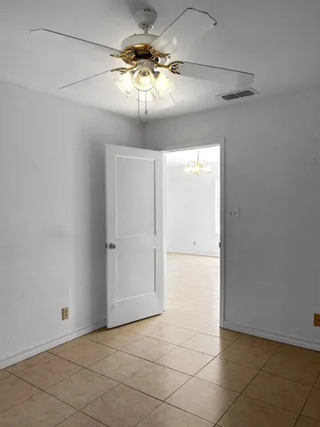 an empty room with a chandelier fan and kitchen view