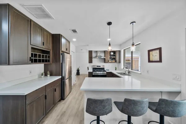 a kitchen with stainless steel appliances a sink a stove a refrigerator cabinets and chairs