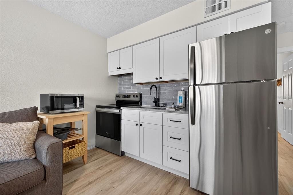 14251 Gulf Boulevard, Unit 5 Madeira Beach, FL 33708 - Photo 9 of 19 a kitchen with white cabinets and stainless steel appliances