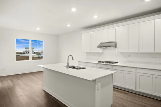 a kitchen with stainless steel appliances granite countertop a sink stove and white cabinets with wooden floor