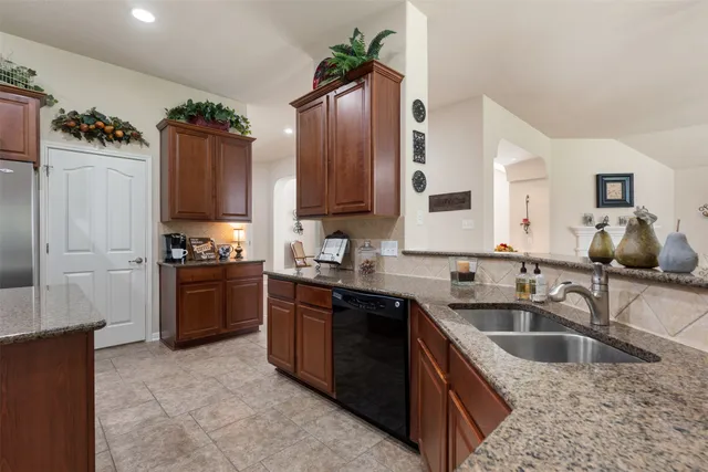 a large kitchen with stainless steel appliances granite countertop a stove a sink dishwasher a refrigerator and a microwave oven with wooden cabinets