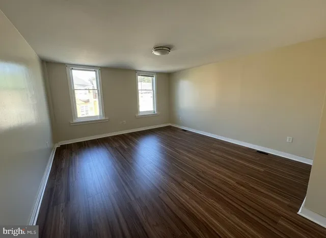 a view of an empty room with wooden floor and window