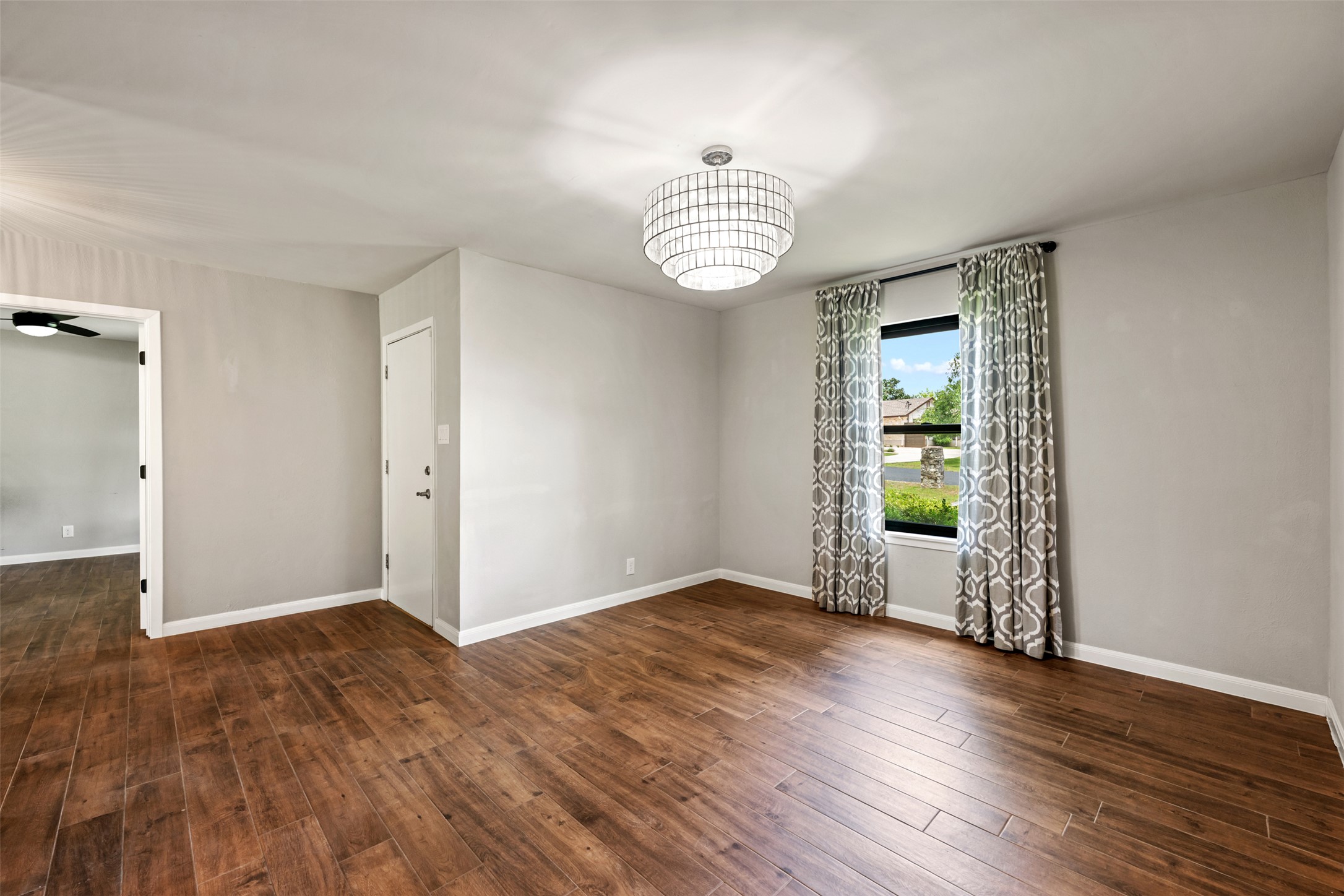 1600 Pin Oak Lane Round Rock, TX 78681 - Photo 9 of 40 Spacious room featuring wood-finish flooring, a modern drum pendant light fixture, a window with patterned drapes, and neutral wall paint