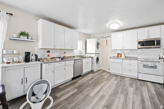 7609 Mountain View Road Lake Point, UT 84074 - Photo 9 of 16 Kitchen featuring appliances with stainless steel finishes, white cabinets, light wood-style floors, estacked washer and dryer, and a textured ceiling