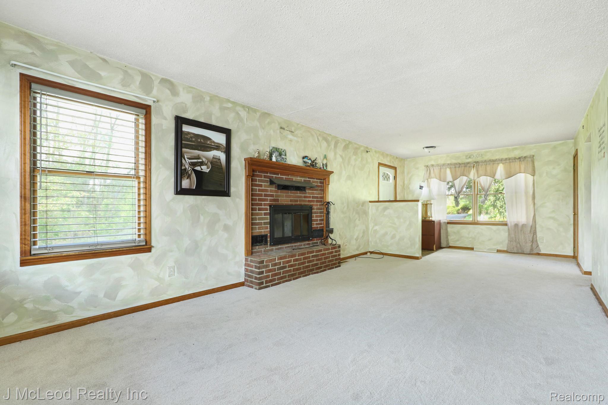69 West Snover Road Mayville, MI 48744 - Photo 10 of 46 Brick fireplace with a wood mantel, light-colored carpet flooring, and two windows with wood-finish trim