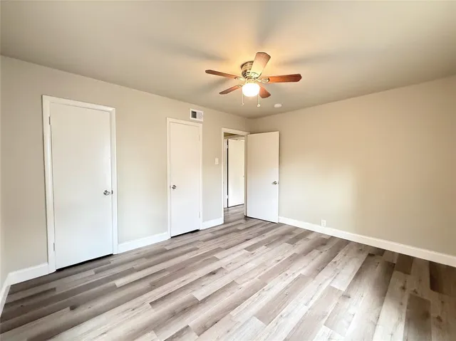 a view of an empty room with wooden floor and a ceiling fan