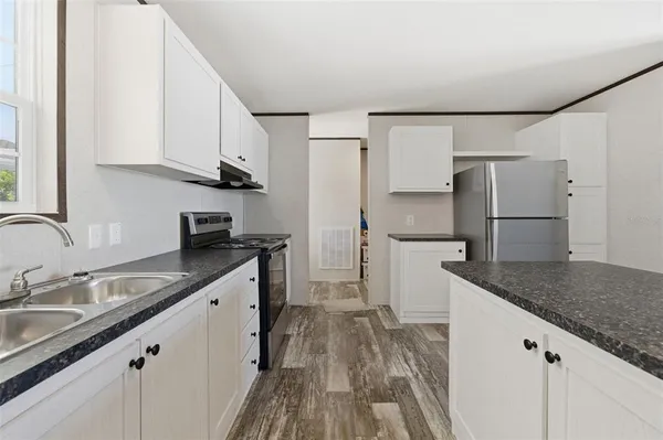 a kitchen with a sink dishwasher a refrigerator and white cabinets with wooden floor