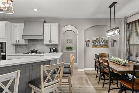 a kitchen with stainless steel appliances granite countertop a dining table chairs stove and white cabinets