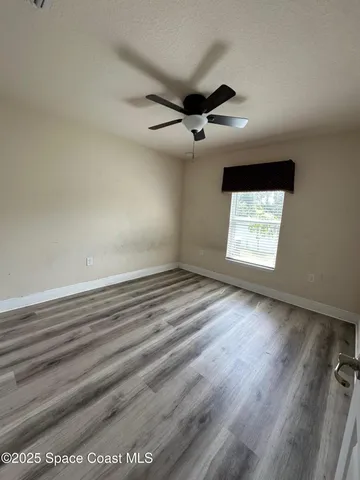 an empty room with wooden floor ceiling fan and windows
