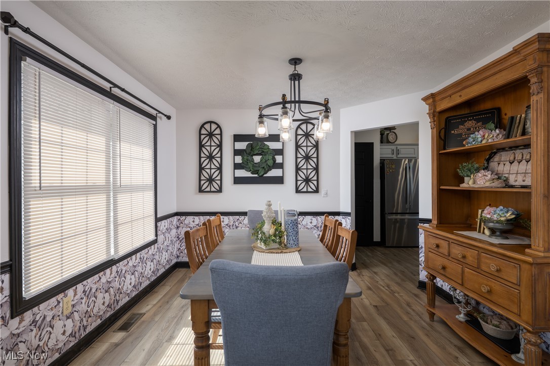 847 Lockwood Road Barberton, OH 44203 - Photo 18 of 29 Dining area featuring wood finished floors, visible vents, wallpapered walls, wainscoting, and a textured ceiling