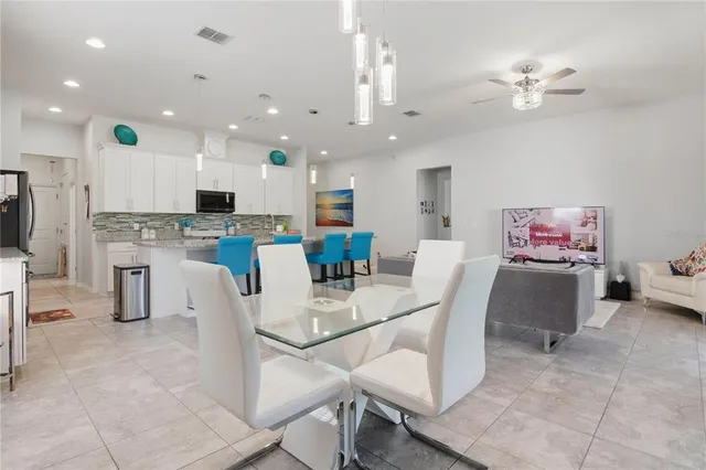 a view of kitchen with stainless steel appliances granite countertop dining table chairs sink and white cabinets