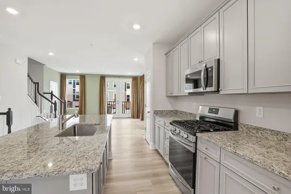 a kitchen with stainless steel appliances granite countertop a stove top oven a sink a refrigerator and white cabinets with wooden floor