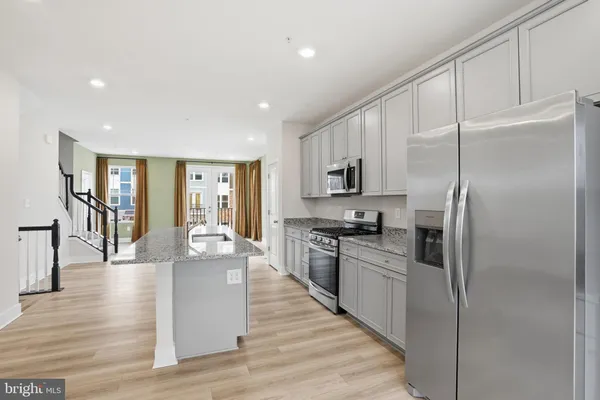 a kitchen with stainless steel appliances granite countertop a refrigerator a stove oven and white cabinets with wooden floors