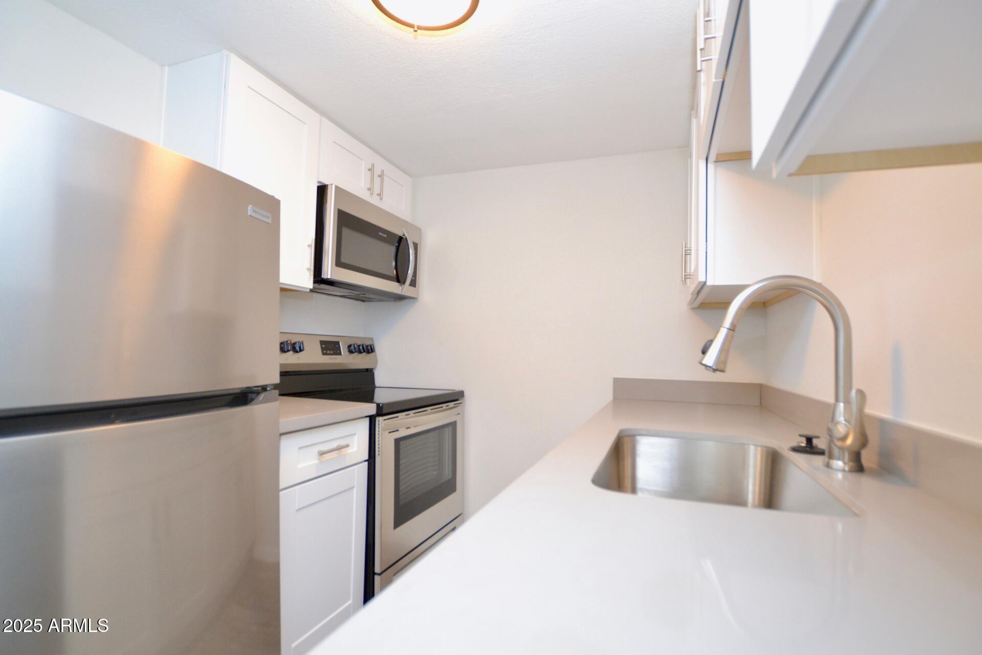 44 East Roanoke Avenue, Unit 8 Phoenix, AZ 85012 - Photo 3 of 11 a kitchen with stainless steel appliances granite countertop a sink a stove top oven and a refrigerator with wooden floor
