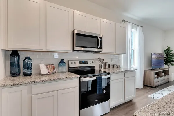 a kitchen with granite countertop white cabinets stainless steel appliances dining table and chairs