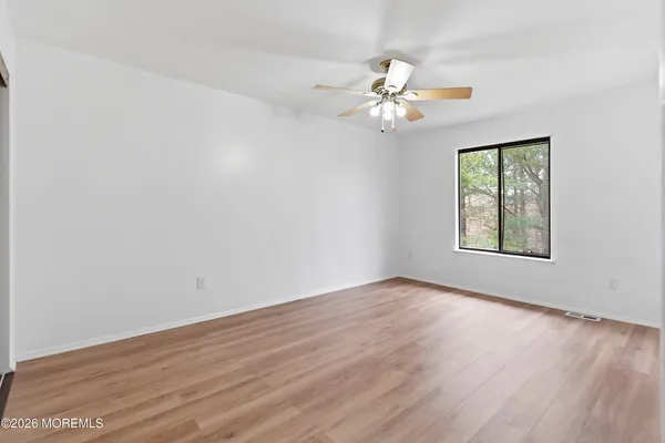 an empty room with wooden floor fan and windows