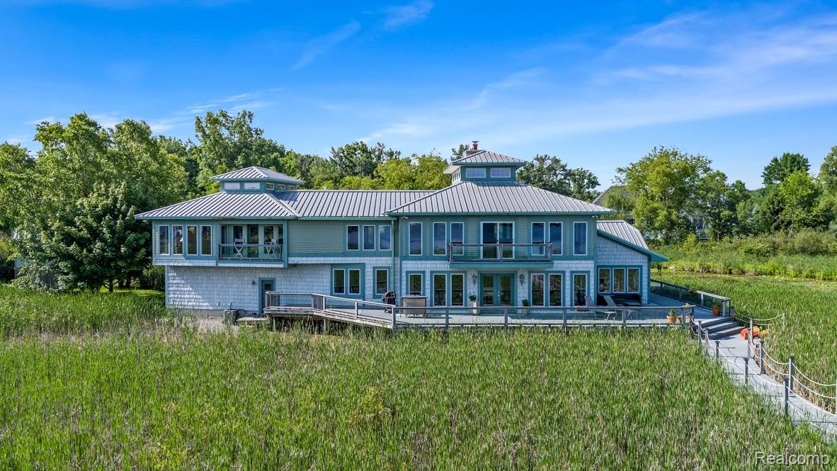 Rear view of property featuring a standing seam roof, a yard, a balcony, and view of wooded area