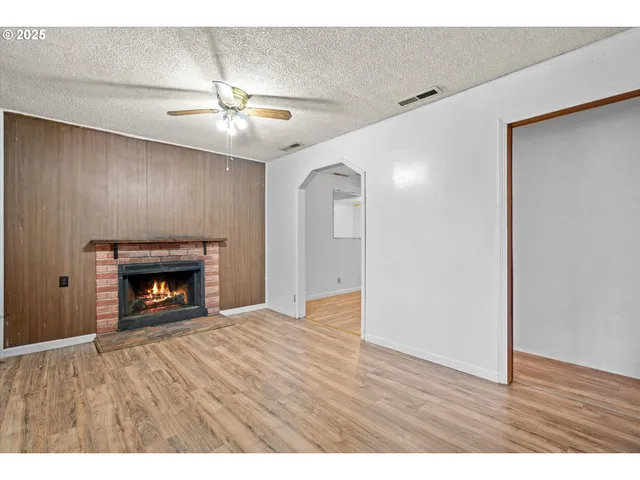 a view of an empty room with wooden floor fireplace and a window