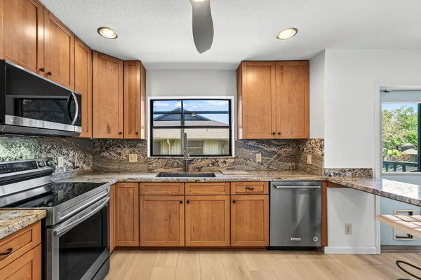 a kitchen with stainless steel appliances granite countertop wooden cabinets a sink a stove a dining table and chairs