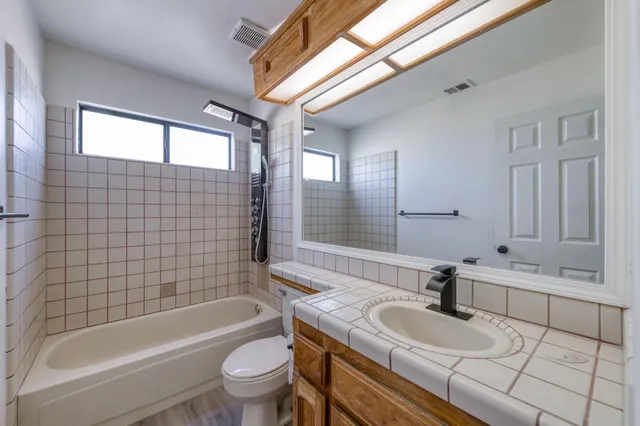 a bathroom with a granite countertop sink a toilet a mirror a bathtub and shower