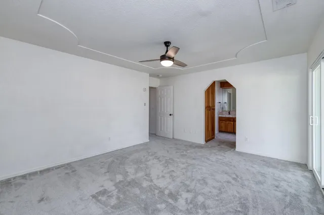 an empty room with chandelier fan and windows