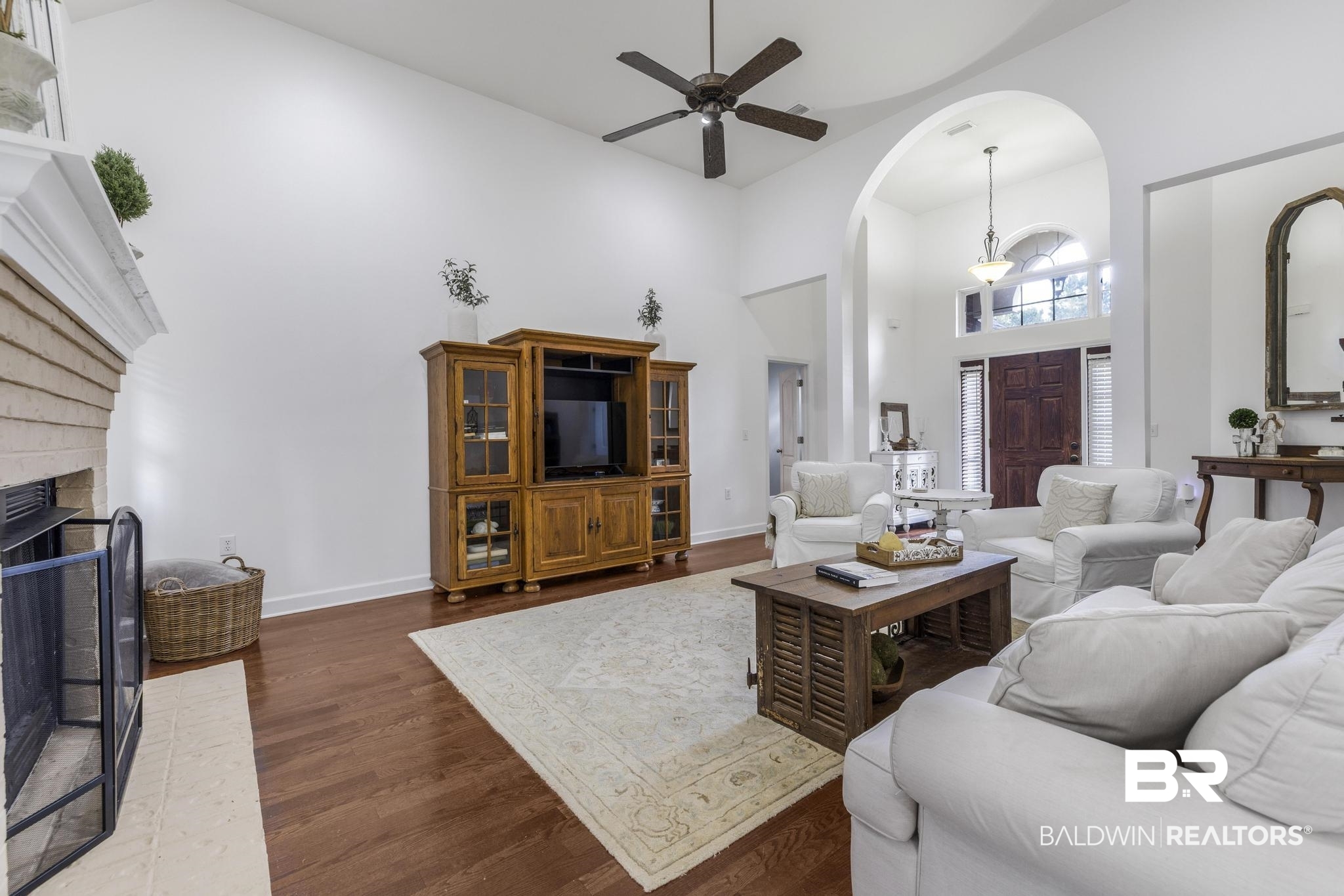 35814 Delvan Lane Bay Minette, AL 36507 - Photo 10 of 53 Living area featuring high vaulted ceilings, wood-finish flooring, a brick fireplace with a white mantel, and an arched entryway leading to the front door