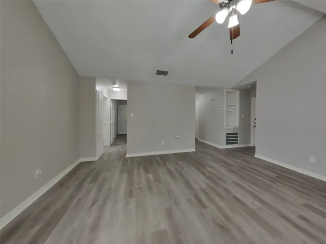 an empty room with wooden floor chandelier fan and windows