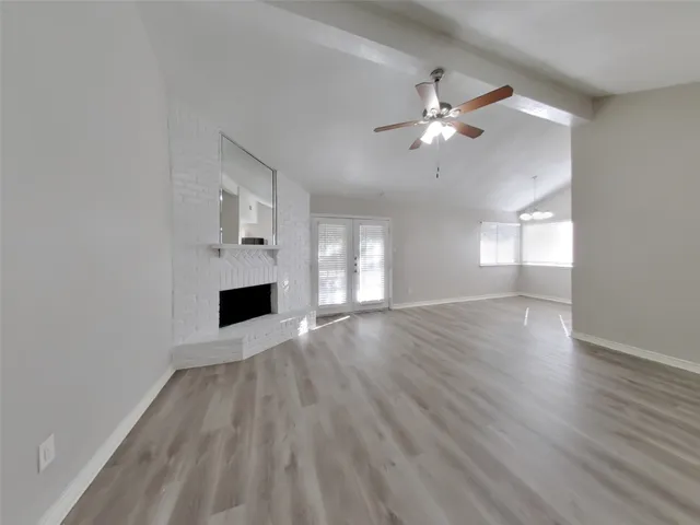 an empty room with wooden floor a ceiling fan a fireplace and windows