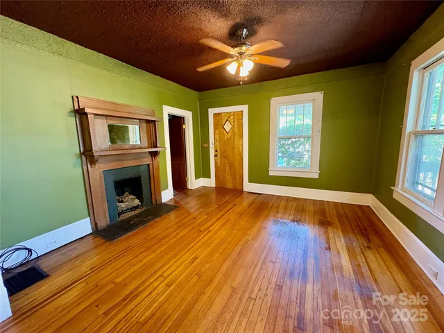 a view of an empty room with wooden floor fireplace and a window