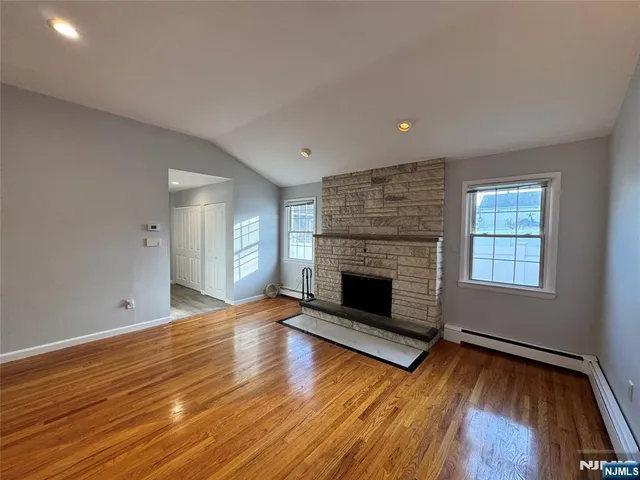 a view of an empty room with wooden floor fireplace and a window