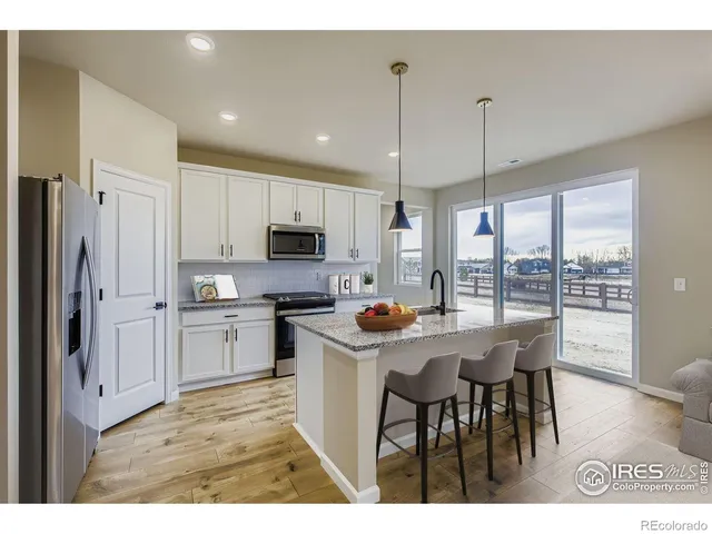 a kitchen with stainless steel appliances kitchen island granite countertop a stove a refrigerator a sink a dining table with chairs and white cabinets next to a window