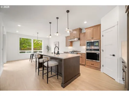 a open kitchen with stainless steel appliances granite countertop a stove top oven a sink dishwasher white cabinets and a dining table with wooden floor
