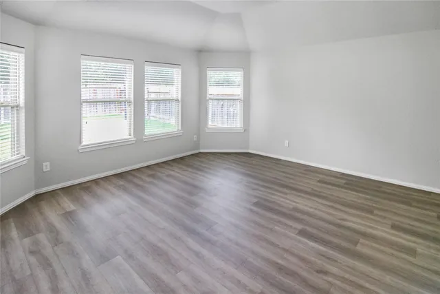 a view of an empty room with wooden floor and window