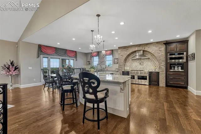 a kitchen with stainless steel appliances granite countertop a kitchen island a stove a dining table and chairs with wooden floor