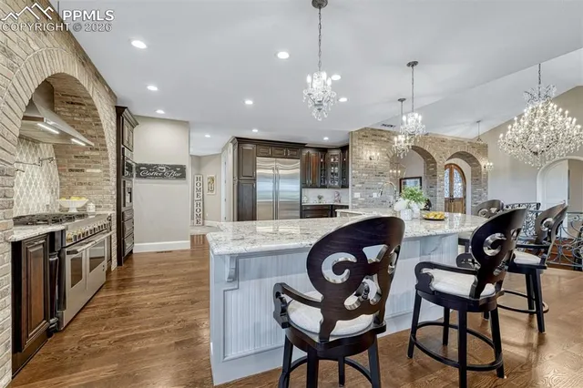 a kitchen with stainless steel appliances granite countertop a stove a sink a refrigerator and chairs