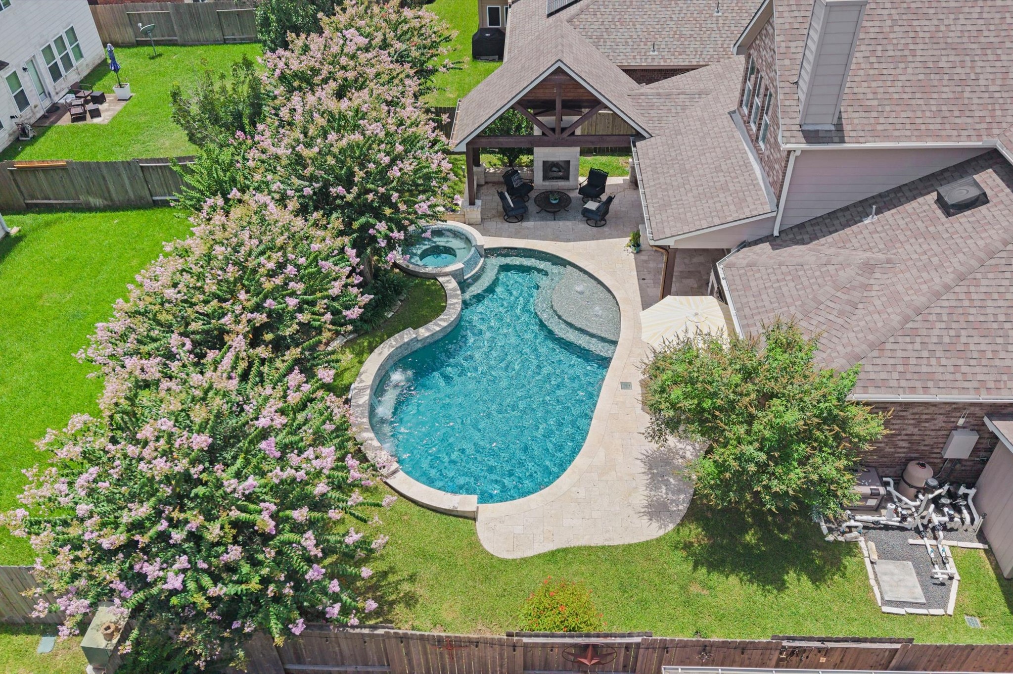 9507 Empress Crossing Drive Spring, TX 77379 - Photo 48 of 50 This aerial view showcases a charming backyard featuring a uniquely shaped pool with a spa, surrounded by lush greenery and flowering trees. There's a covered patio area attached to the house, perfect for outdoor entertaining. The space is fenced in, offering privacy and a serene environment.