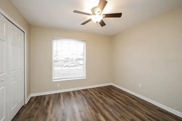 an empty room with wooden floor ceiling fan and windows