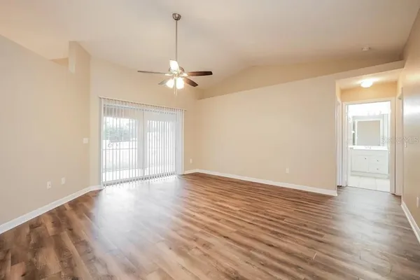 a view of an empty room with wooden floor and a ceiling fan