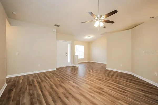 a view of an empty room with wooden floor and a ceiling fan