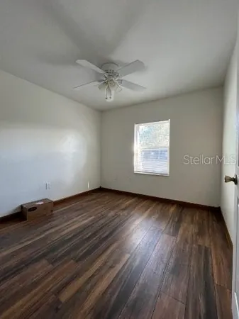 an empty room with wooden floor chandelier fan and windows