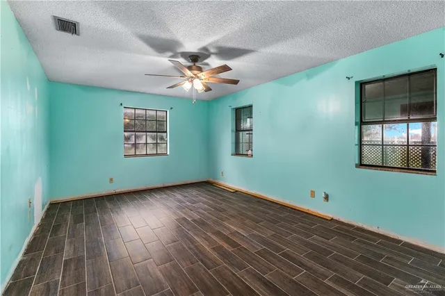an empty room with wooden floor chandelier fan and windows
