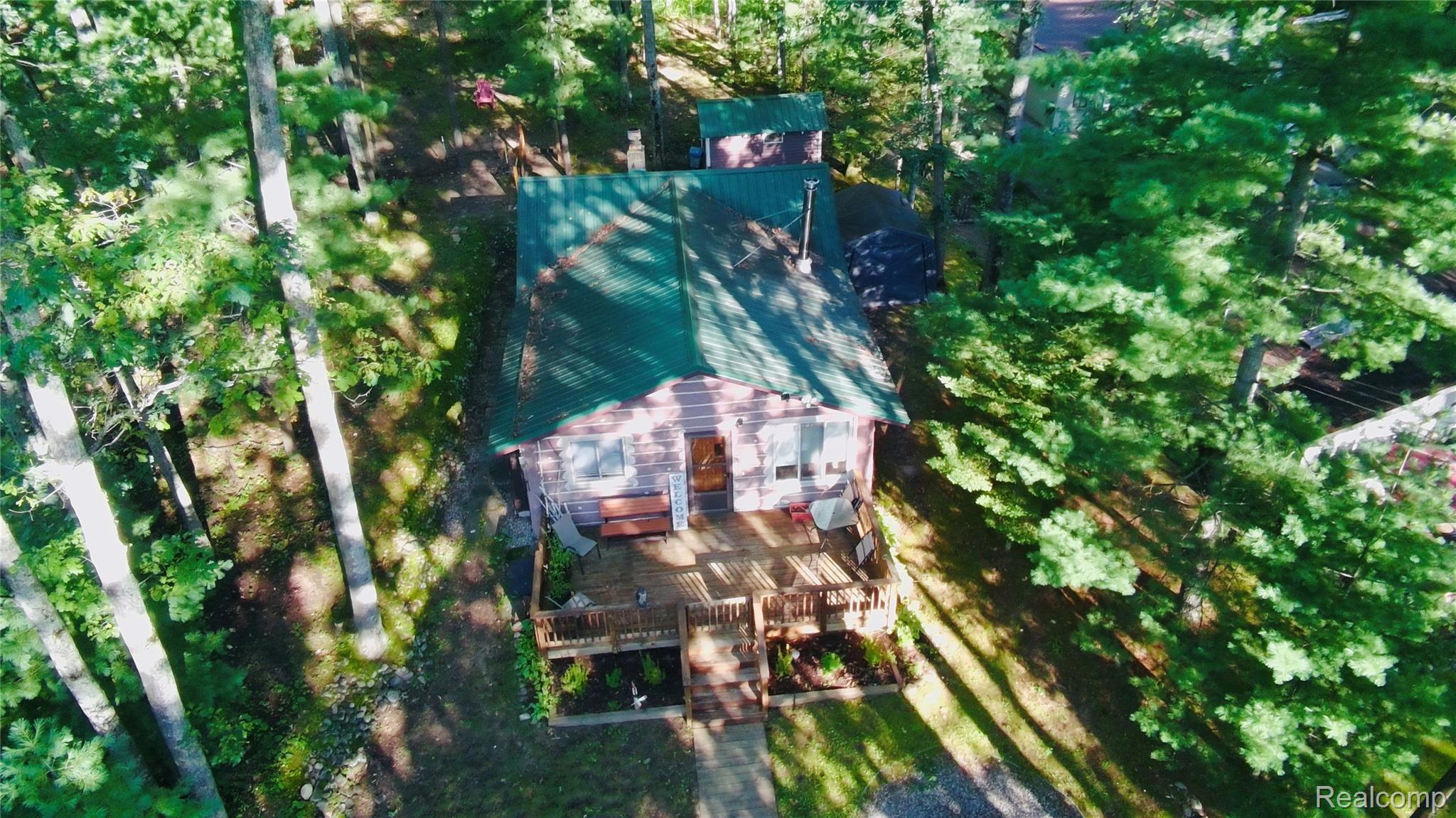 417 Ogemaw Road Rose City, MI 48654 - Photo 18 of 26 Wood-sided exterior with a green metal roof, front deck, and surrounding mature trees