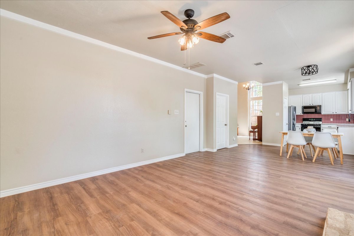 9300 Tea Rose Trail Austin, TX 78748 - Photo 17 of 33 An inviting open-concept living space features warm wood-look flooring and a functional ceiling fan, flowing seamlessly into a modern kitchen.