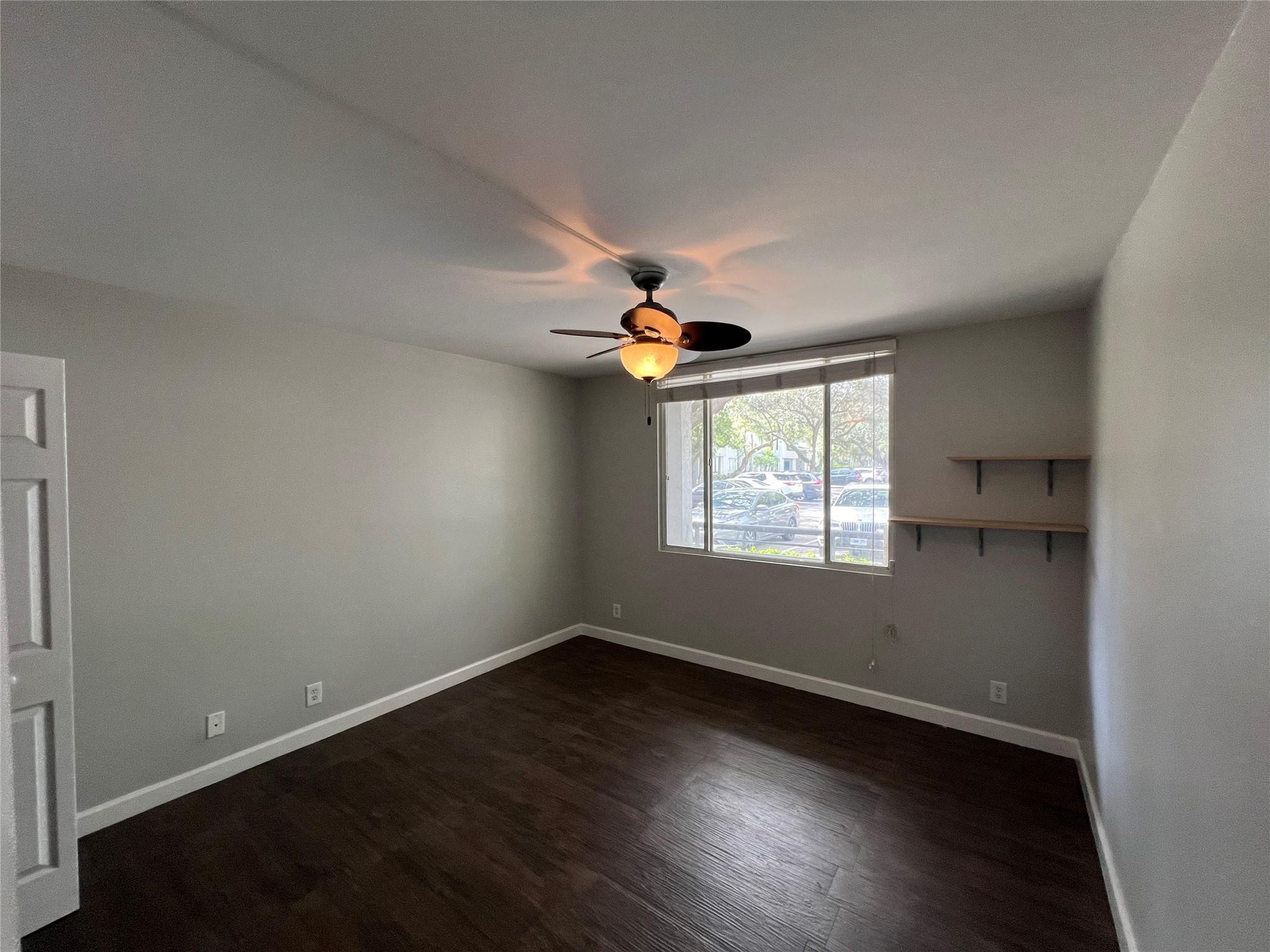 921 Lyons Road, Unit 3105 Coconut Creek, FL 33063 - Photo 11 of 28 an empty room with wooden floor chandelier fan and windows