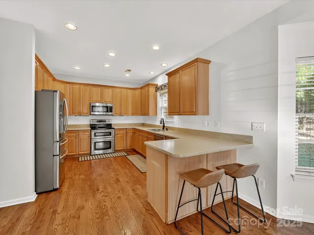 a kitchen with stainless steel appliances granite countertop a refrigerator a sink dishwasher a stove with wooden cabinets and floor