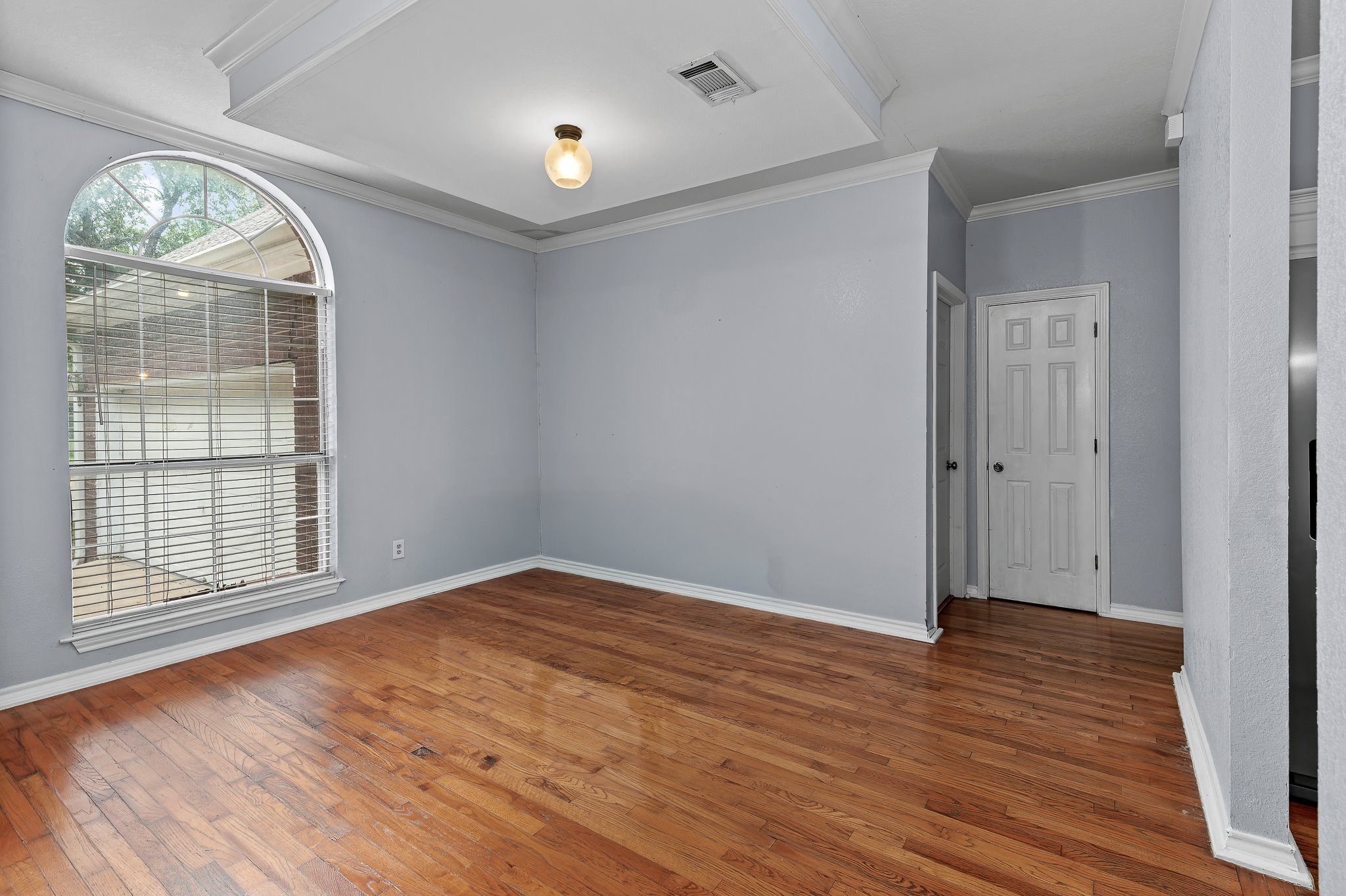 11737 Rydalwater Lane Austin, TX 78754 - Photo 6 of 40 Spacious room featuring hardwood flooring, a large arched window with blinds, a tray ceiling, and crown molding