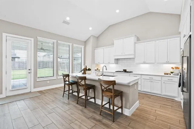 a open dining room with kitchen island granite countertop a sink and white cabinets with wooden floor